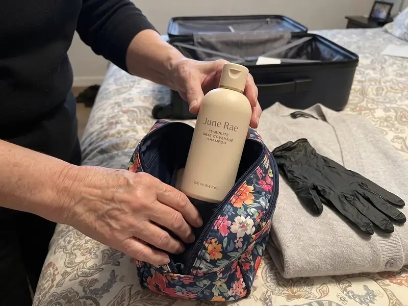 A woman in her sixties packing a cream shampoo bottle into a travel toiletry bag